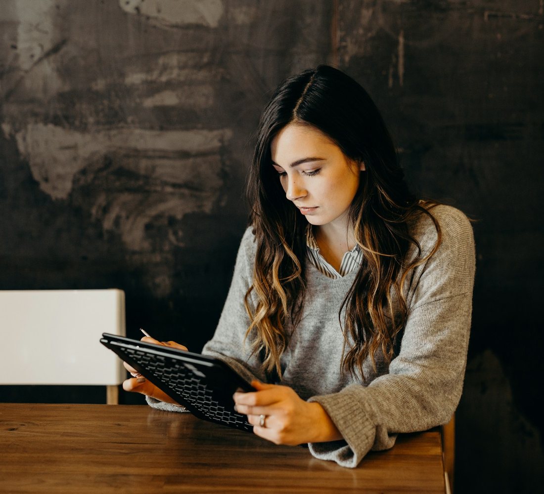 Une jeune femme concentrée sur sa tablette à une table