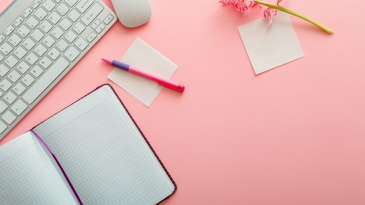 Bureau rose avec un carnet ouvert, un stylo et des notes